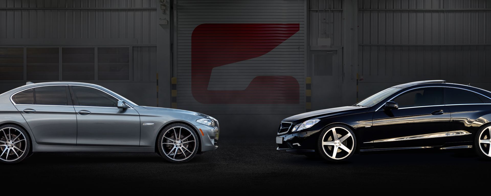 Two cars, a silver sedan and a black coupe, parked in front of a gray garage with a red logo. | Gravity Service Center