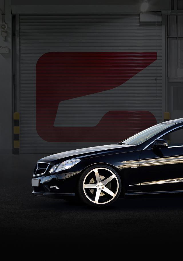 Black Mercedes-Benz sedan parked in front of a garage with a large red logo. | Gravity Service Center