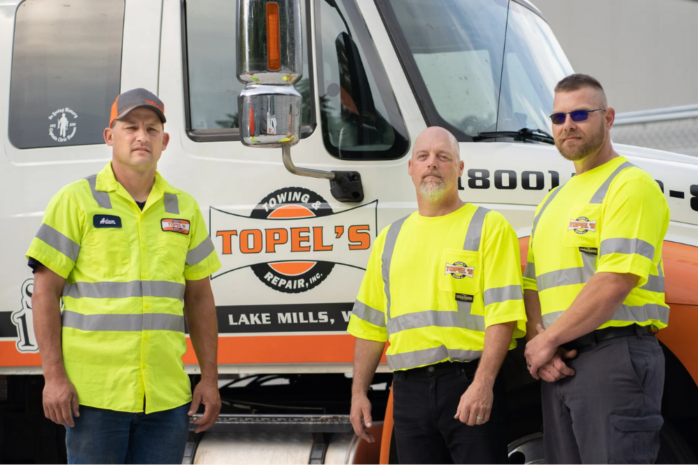 Topel's Towing & Repair team in Lake Mills, WI, standing in front of a branded tow truck.