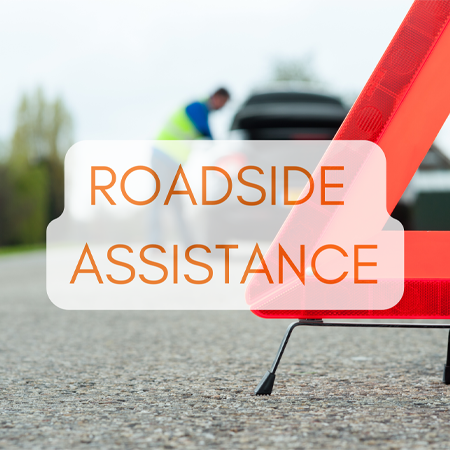 Towing service station in Lake Mills, WI? Topel's Towing & Repair, Inc. A close-up of a safety triangle on the road with a blurred background of a person providing roadside assistance to a vehicle.