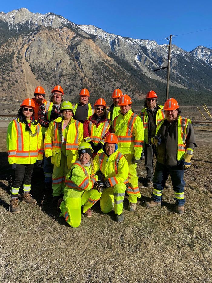 A group of construction workers are posing for a picture in front of a mountain.