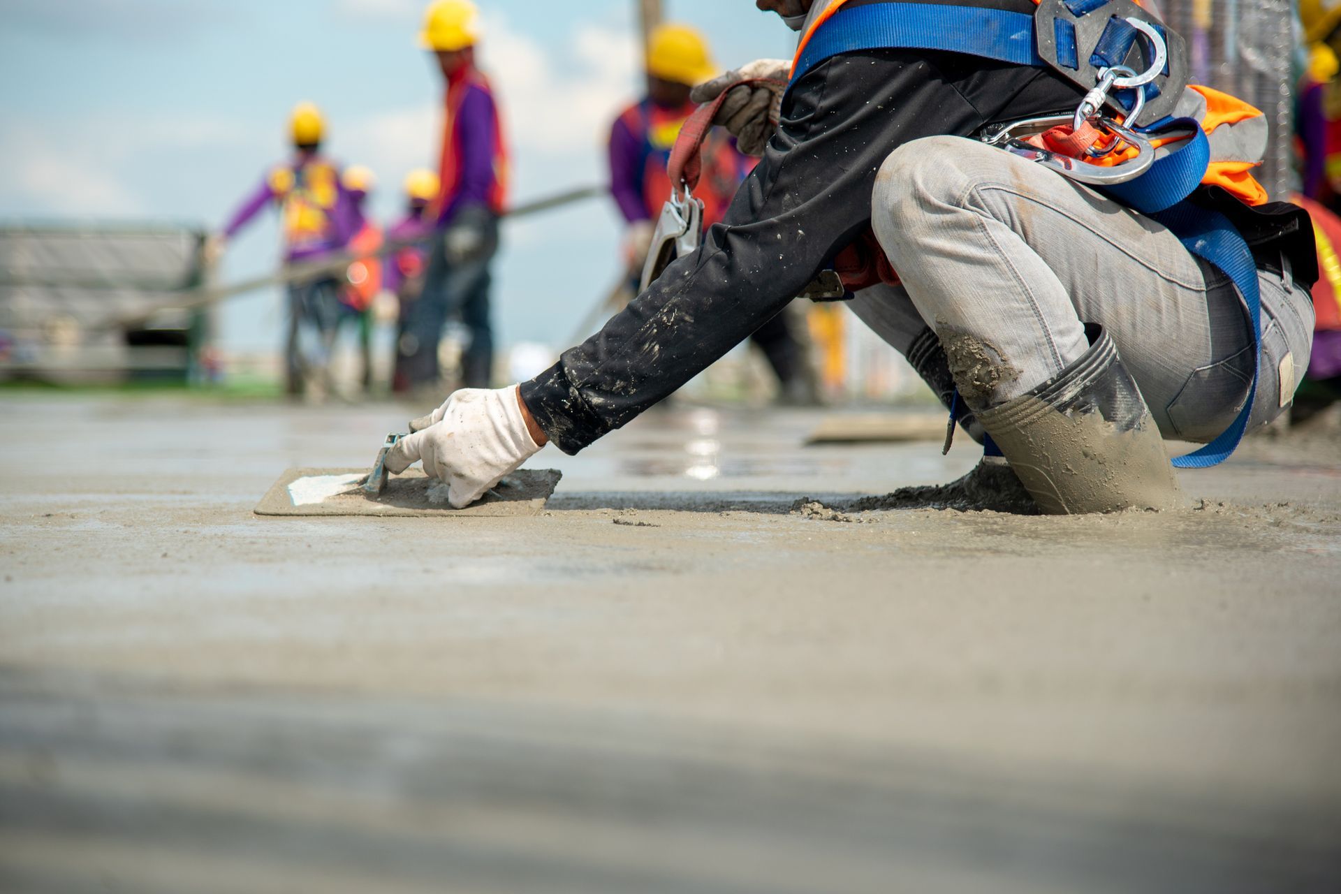 A construction worker is kneeling down and spreading concrete on the ground.