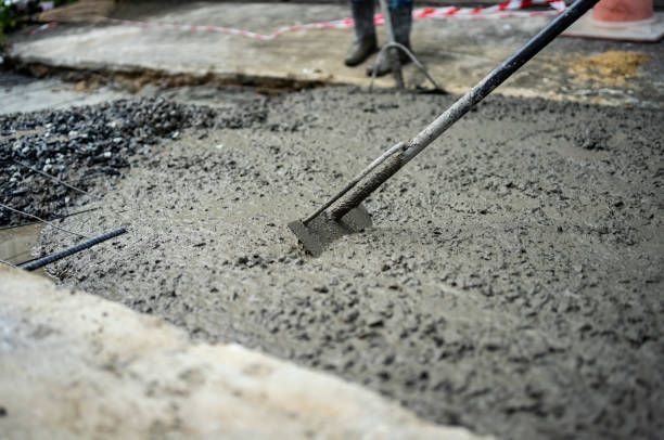 A person is spreading concrete on the ground with a shovel.