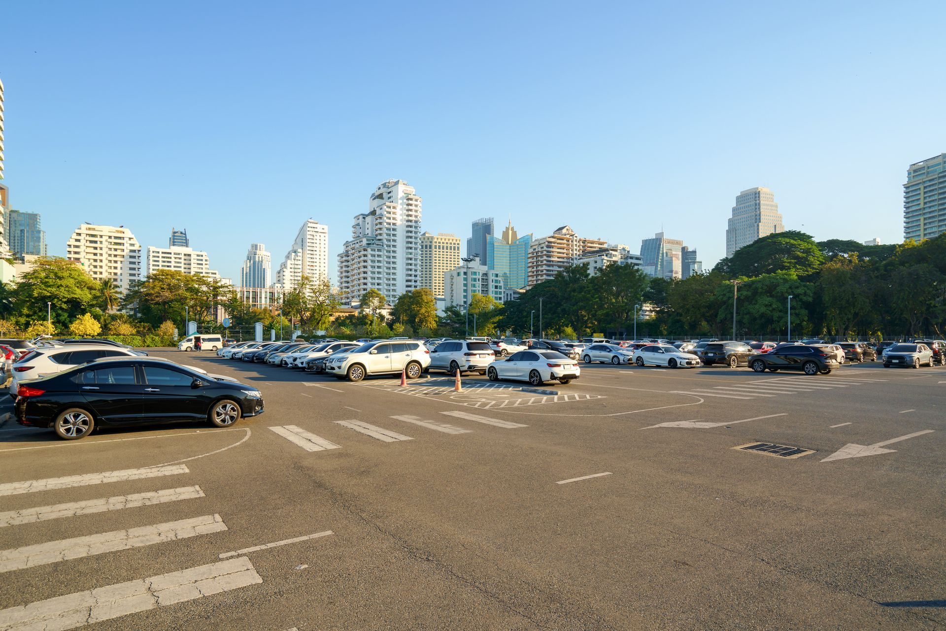 A lot of cars are parked in a parking lot with a city in the background.