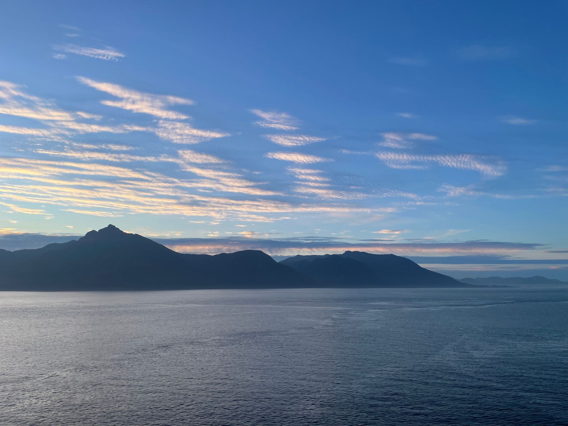 A large body of water with mountains in the background and a blue sky with clouds.