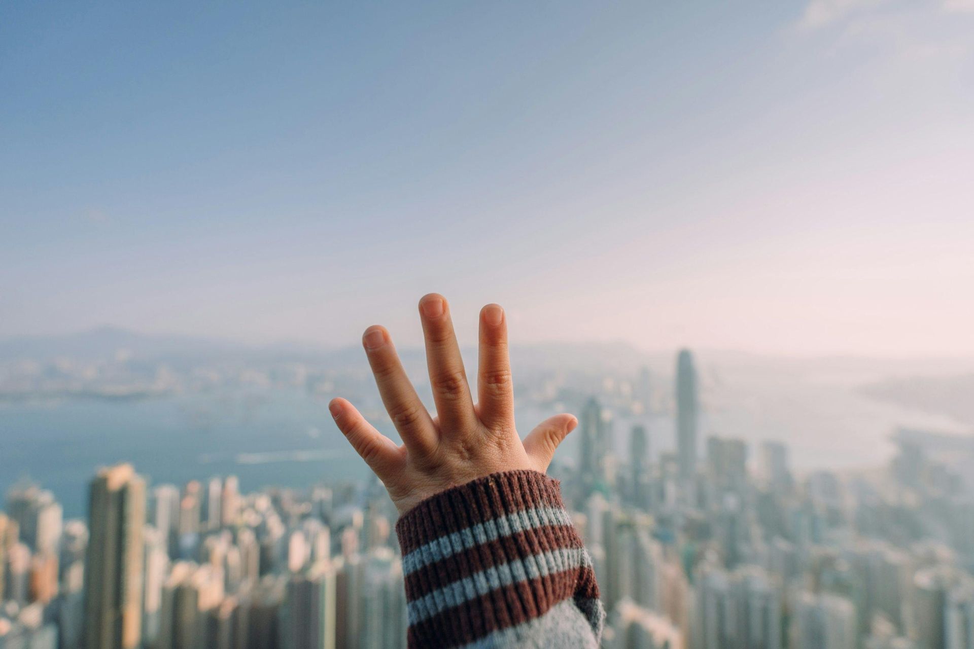 A child is reaching out their hand in front of a city skyline.