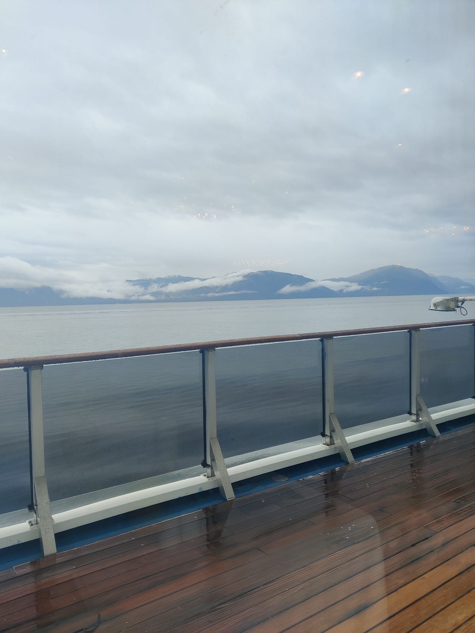 A view of the ocean from the deck of a cruise ship, Alaskan mountains in distance.