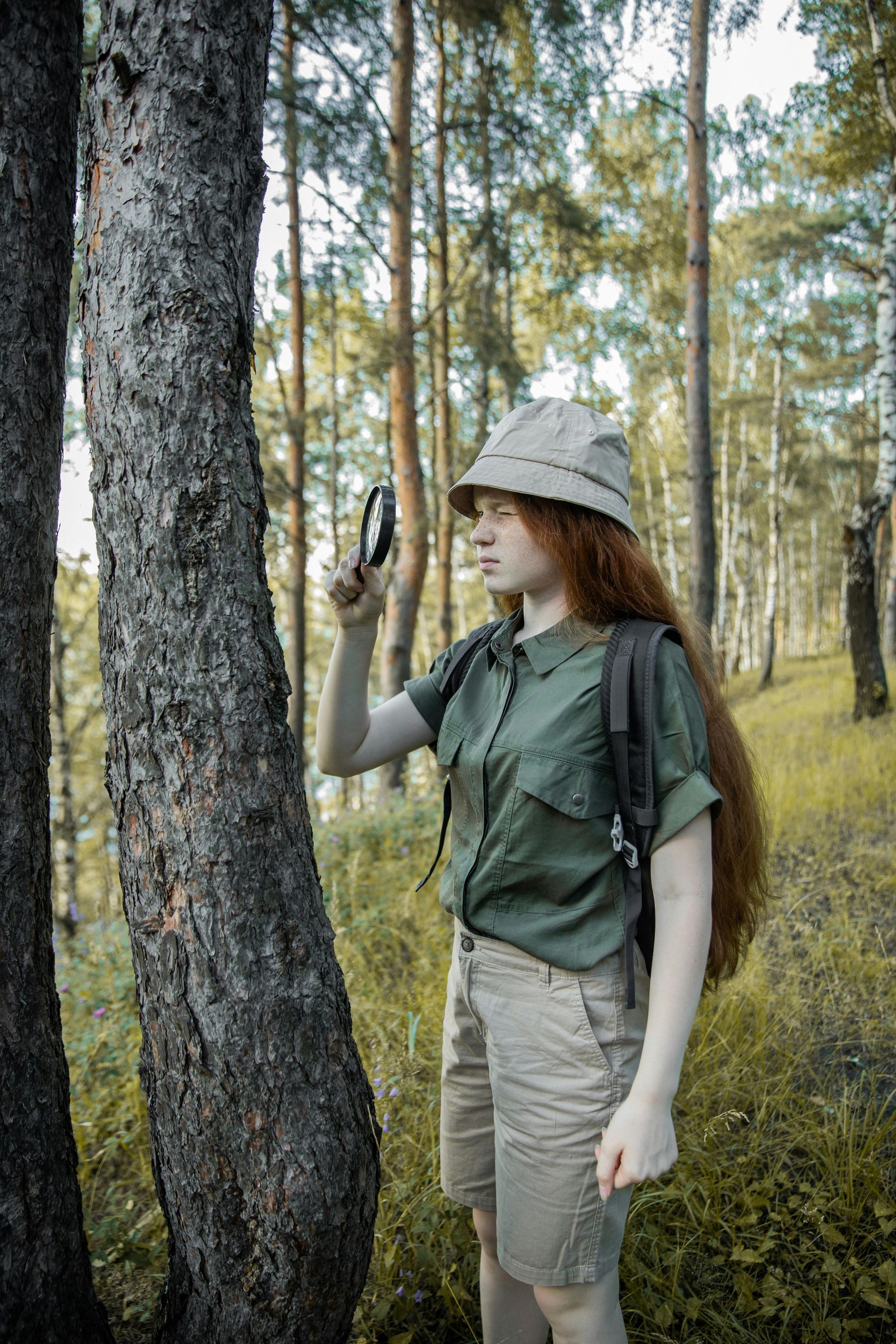 A girl looking through a magnifying glass at a tree in the woods.