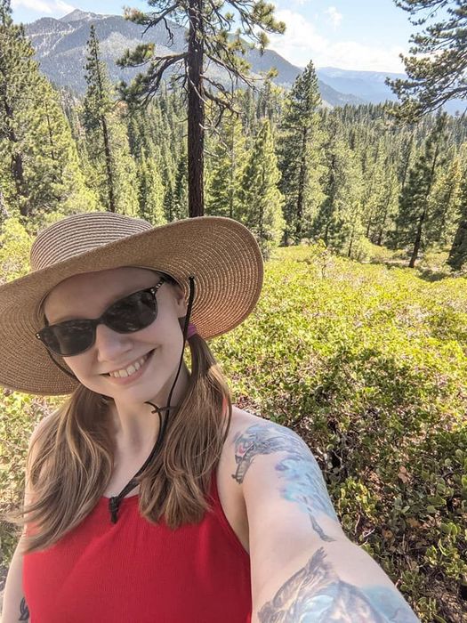 Selfie of Hailey on a trail up in the Tahoe region on a sunny day; very green background.