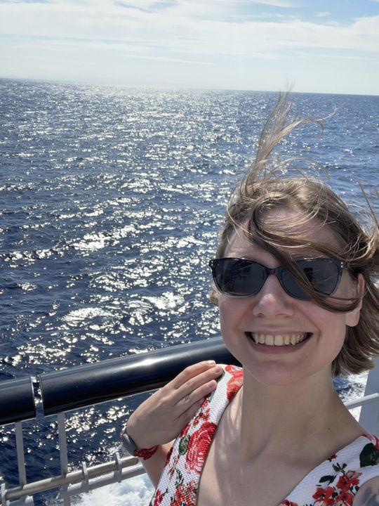 Selfie of Hailey on the side of a cruise ship on a sunny, windy day, while wearing sunglasses