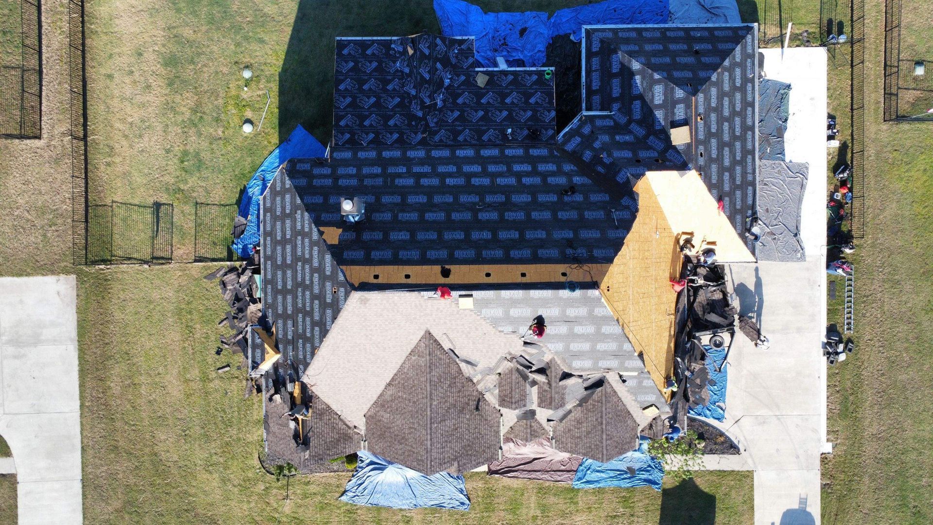 An aerial view of a house under construction with a blue tarp on the roof.
