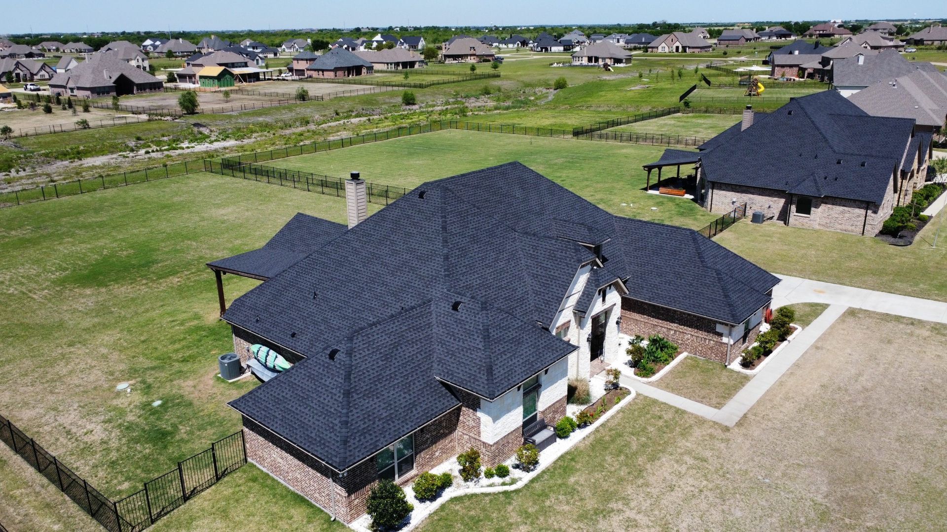 An aerial view of a house with a black roof in a residential area.