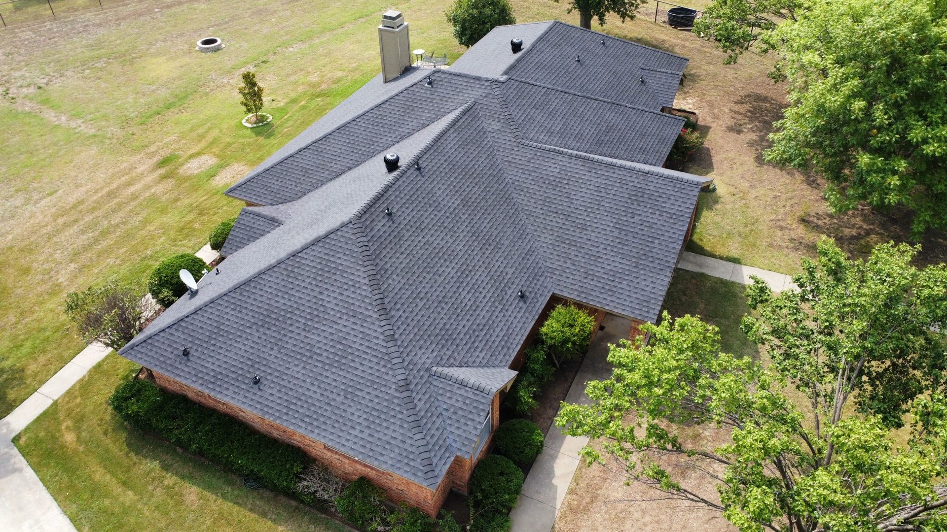 An aerial view of a house with a black roof surrounded by trees and grass.