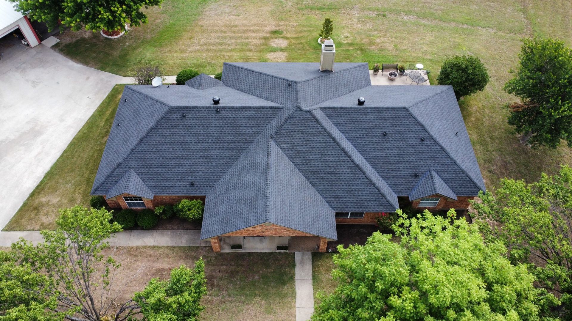 An aerial view of a large house with a black roof surrounded by trees.