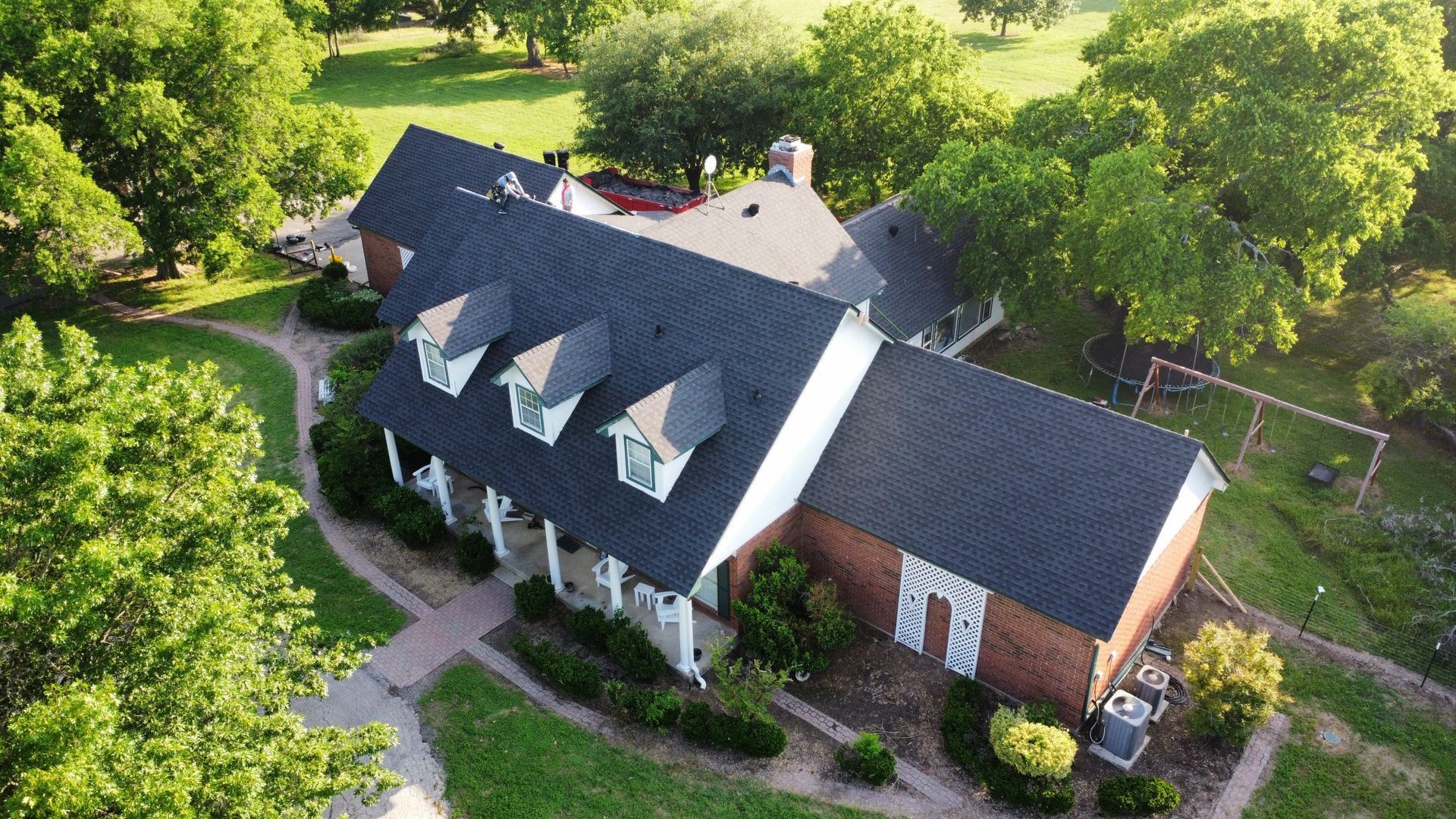 An aerial view of a large brick house with a black roof surrounded by trees.