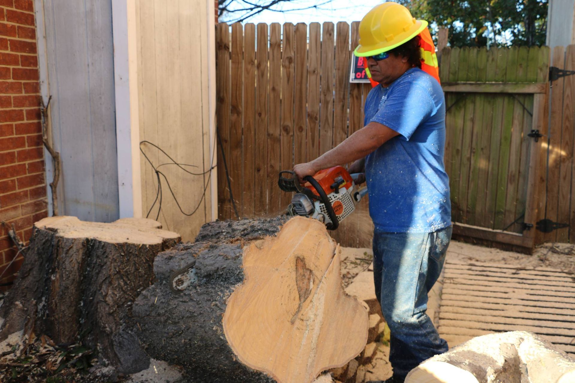 A man wearing a hard hat is cutting a tree stump with a chainsaw.