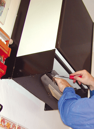 A man in blue overalls repairing a brown and cream boiler with a red screwdriver