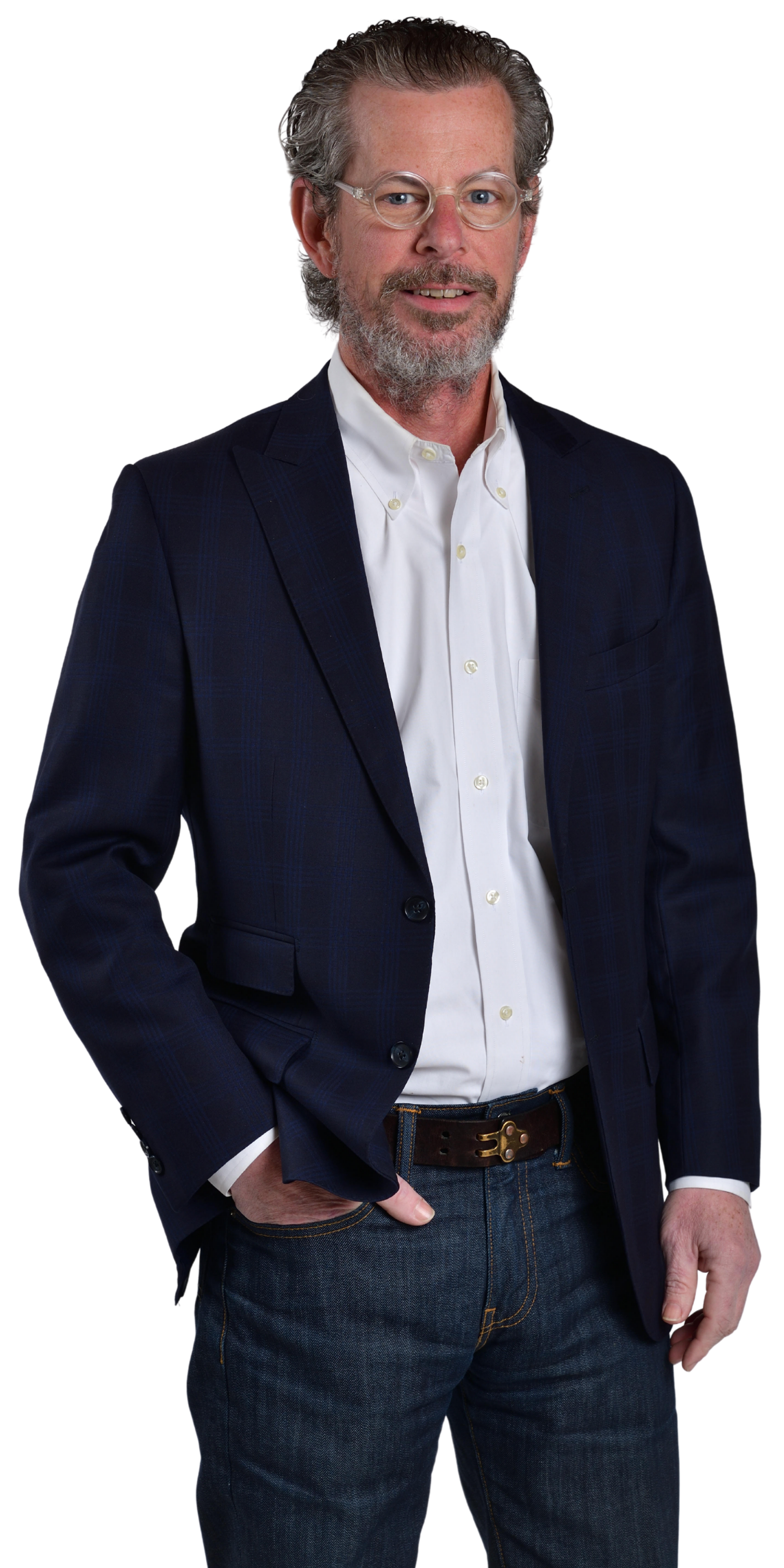 Man in a navy blazer, white shirt, and jeans, with glasses and a beard, standing and posing with his hand in his pocket.