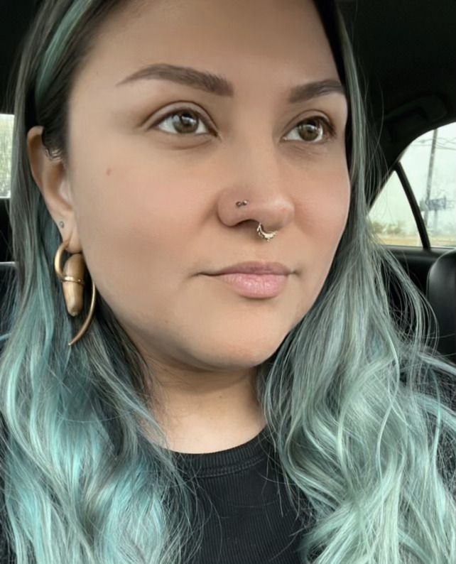a woman with blue hair and a nose ring is sitting in a car .