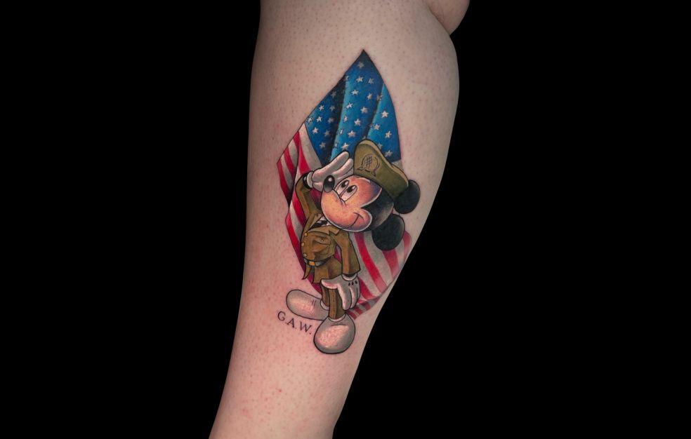 a tattoo of mickey mouse in a military uniform saluting an american flag .