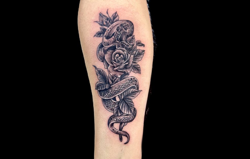a black and white tattoo of a snake and roses on a person 's arm .