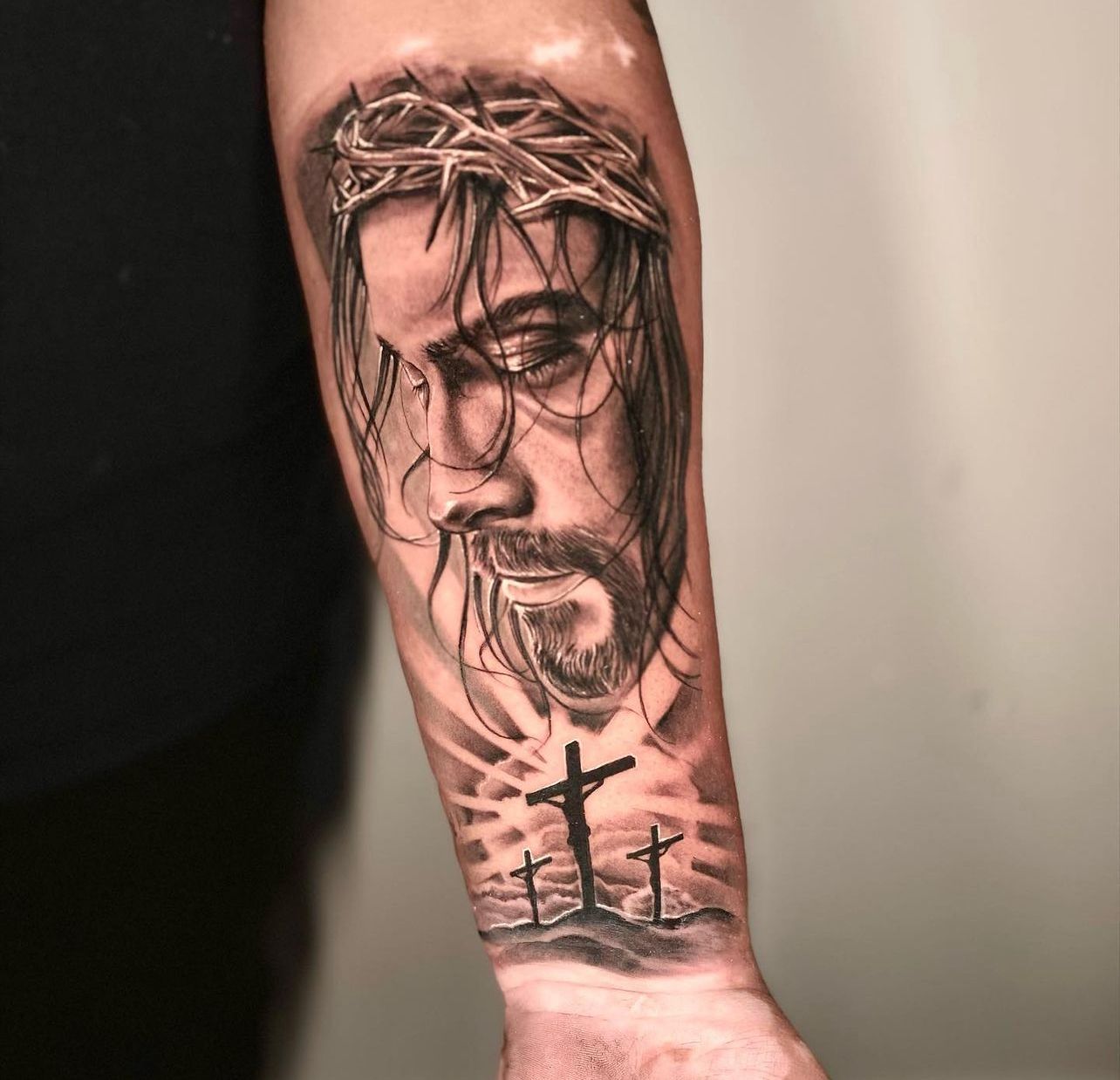 a man has a tattoo of jesus with a crown of thorns and crosses on his forearm .