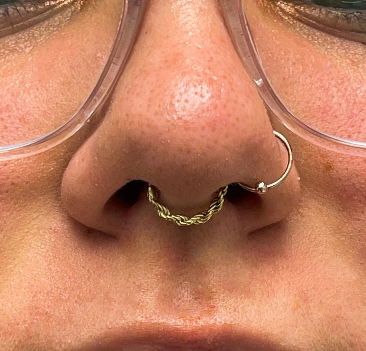 a close up of a woman 's nose with a nose ring and glasses .