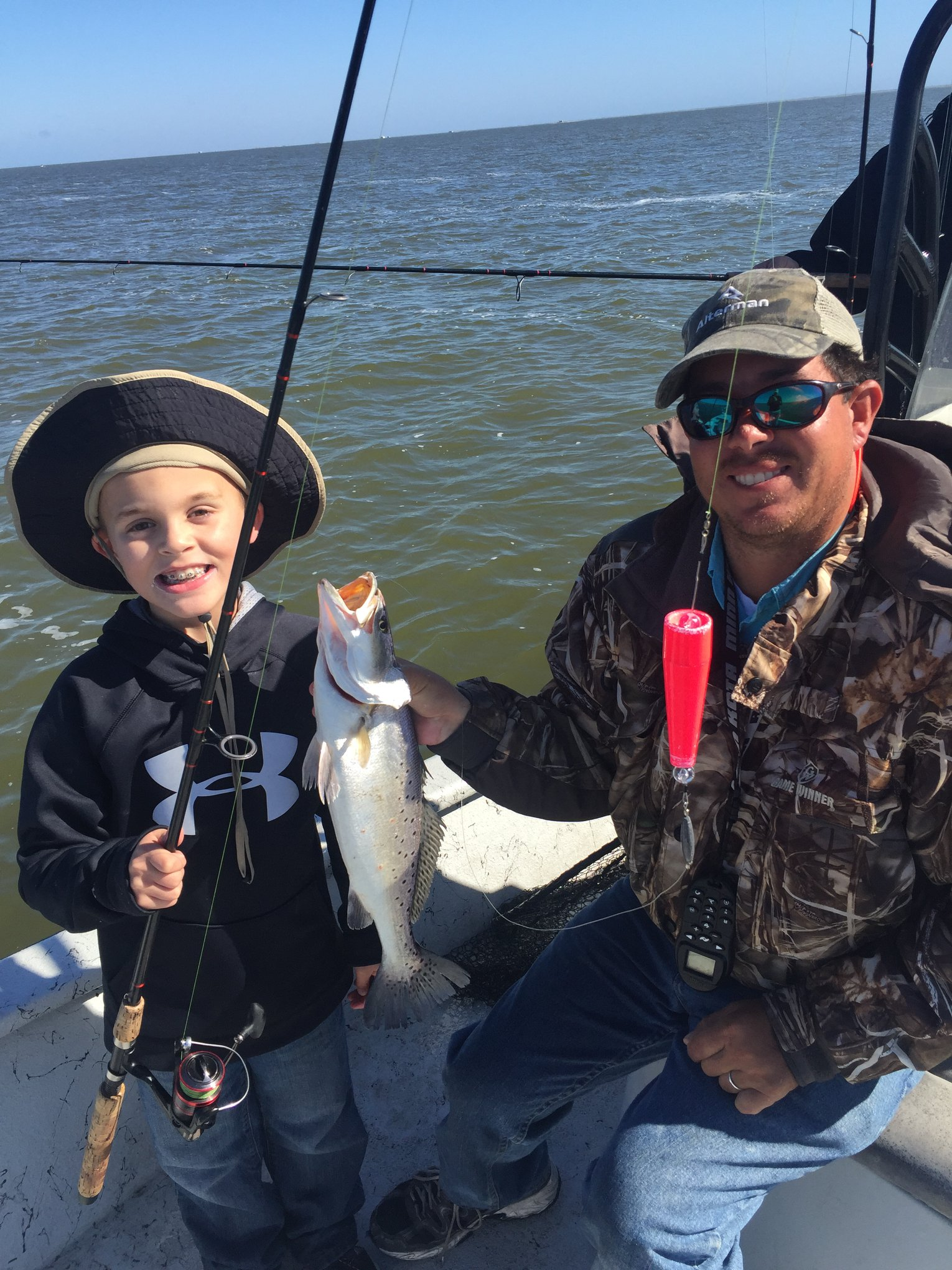 A man and a boy are fishing on a boat and the boy is holding a fish.