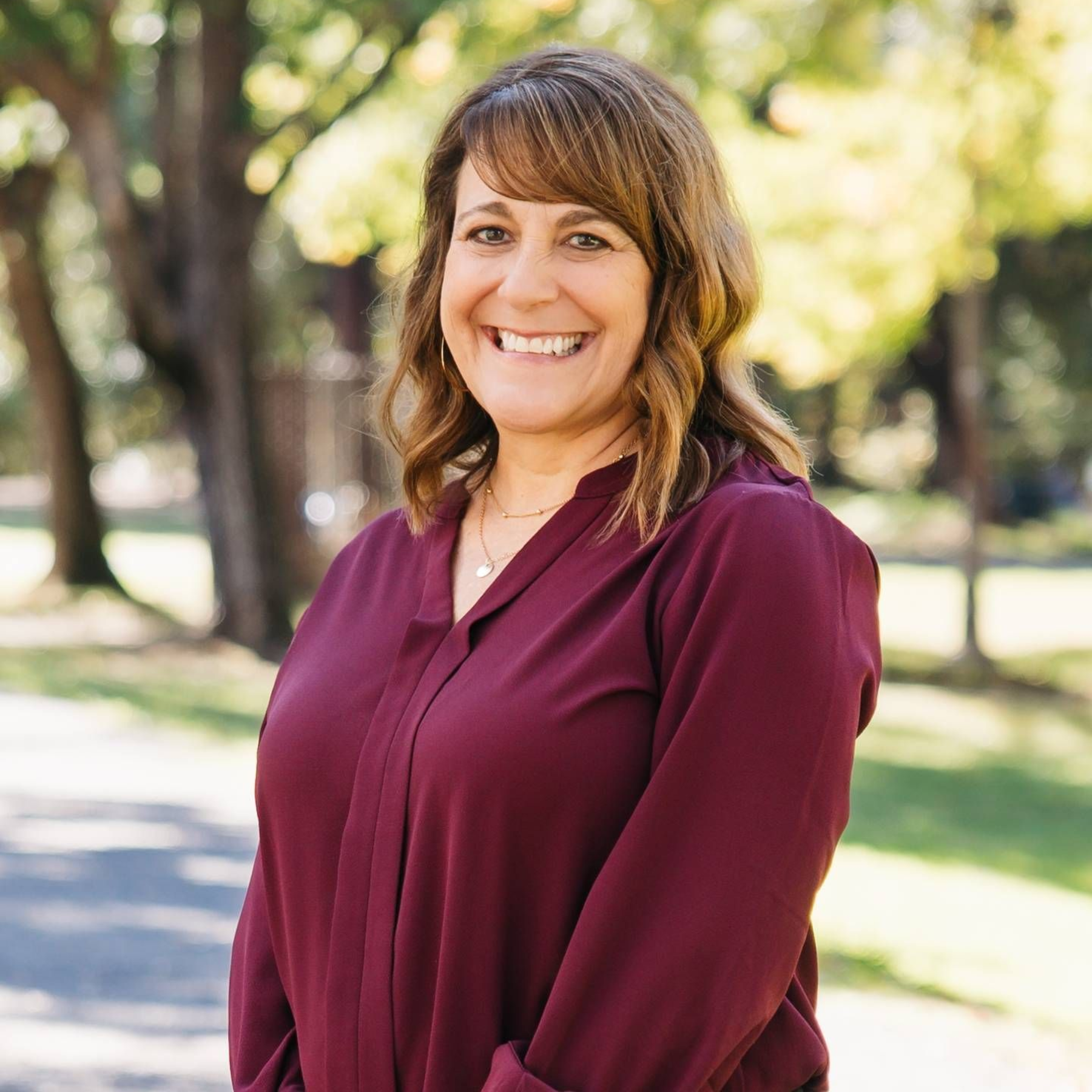 A woman wearing a black jacket and a necklace smiles for the camera