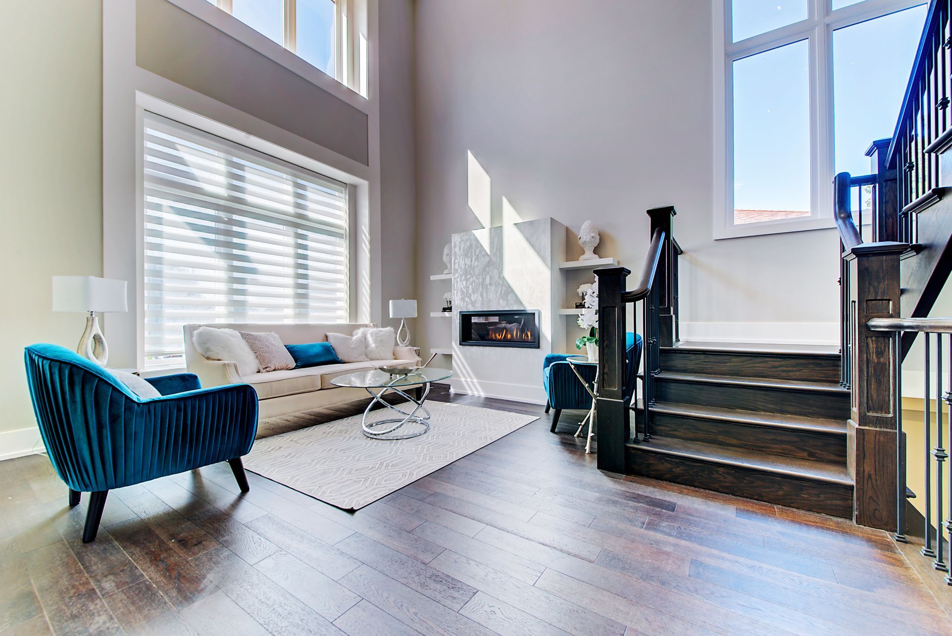 A living room with a couch , chairs , stairs and a fireplace.