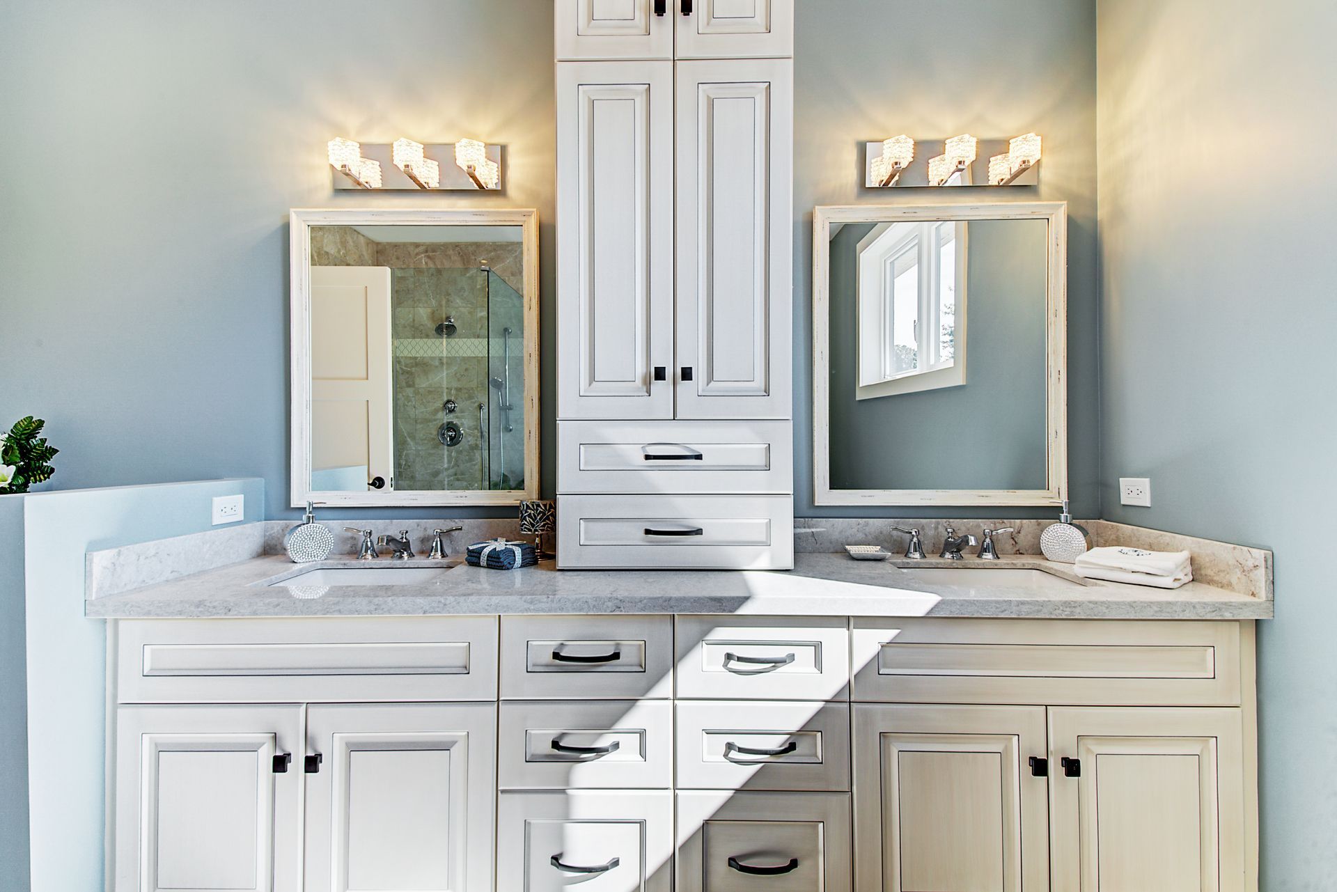 A bathroom with two sinks , two mirrors , and white cabinets.