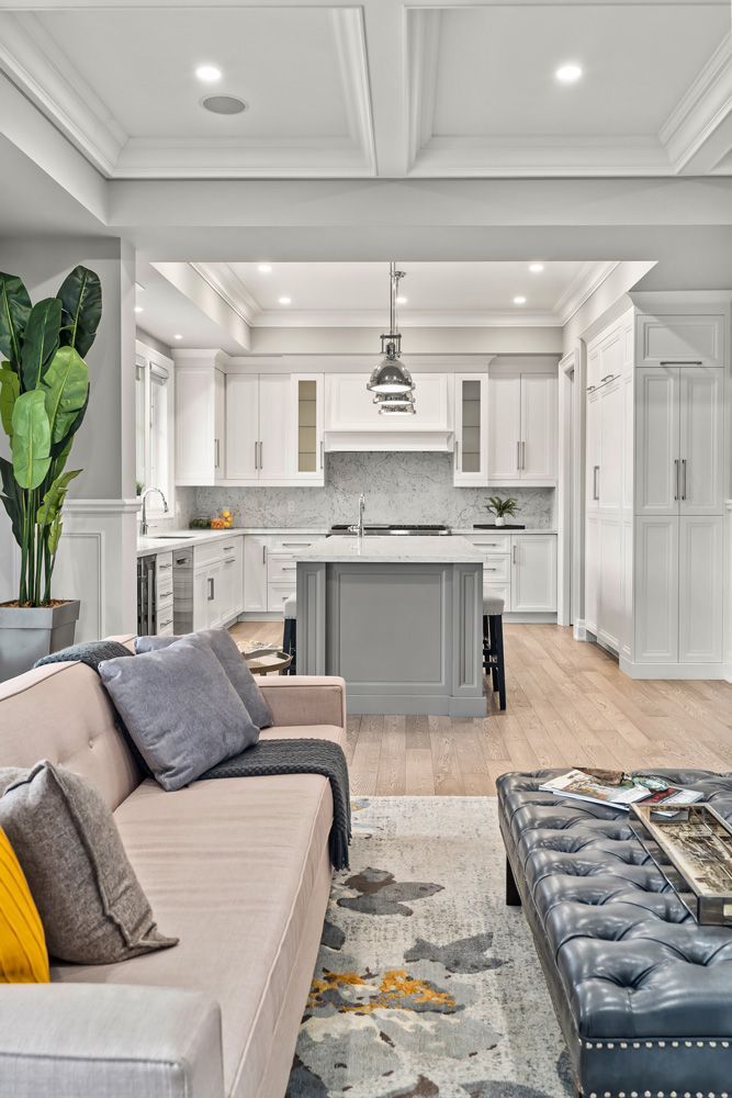 A living room with a couch and ottoman and a kitchen in the background on Tansley Drive by Oakroots Construction