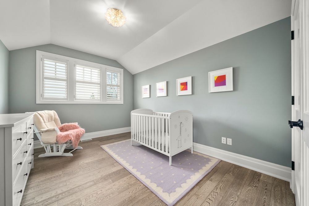 A nursery with a crib, rocking chair, and dresser on Tansley Drive by Oakroots Construction