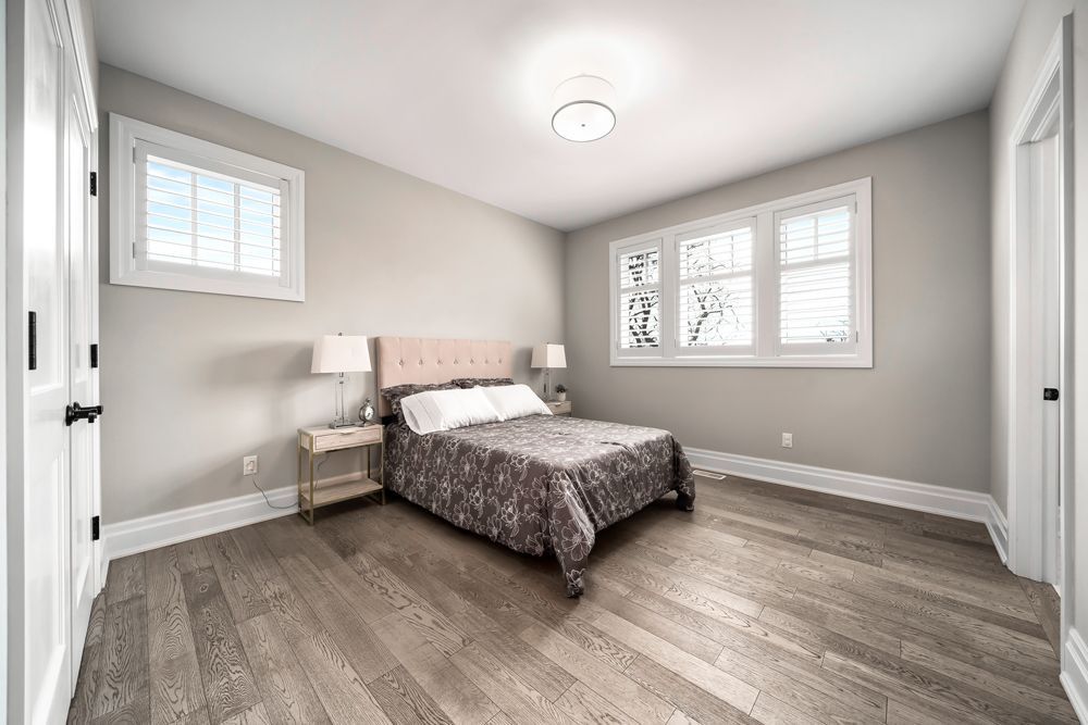 A bedroom with a bed, lamps, windows and hardwood floors on Tansley Drive by Oakroots Construction