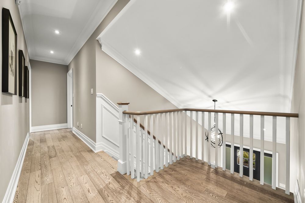 A hallway with hardwood floors and a staircase in a house on Tansley Drive by Oakroots Construction