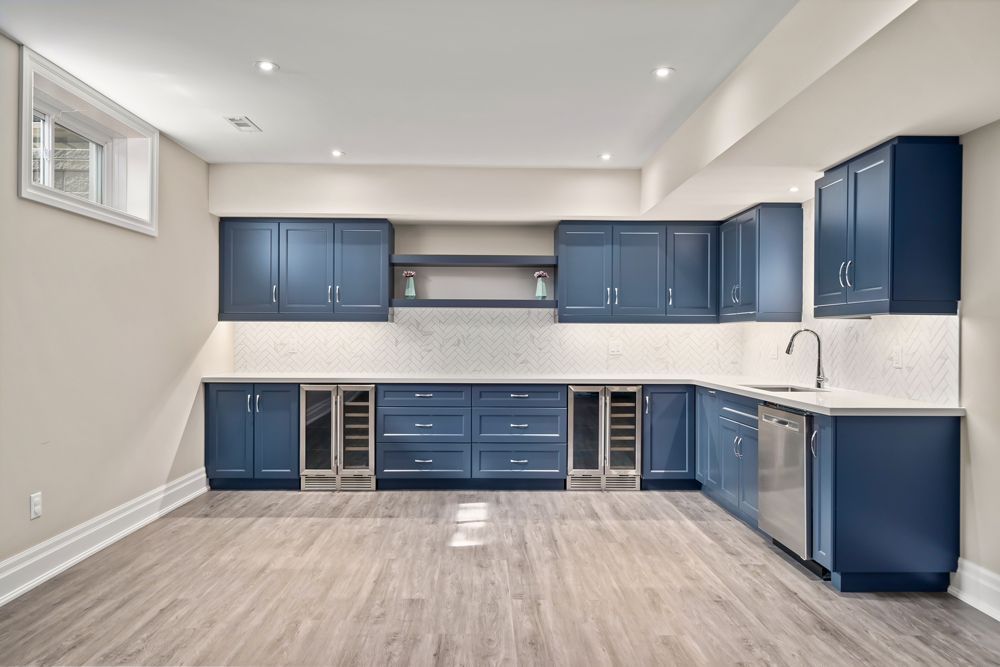 An empty basement with blue cabinets and stainless steel appliances on Tansley Drive by Oakroots Construction