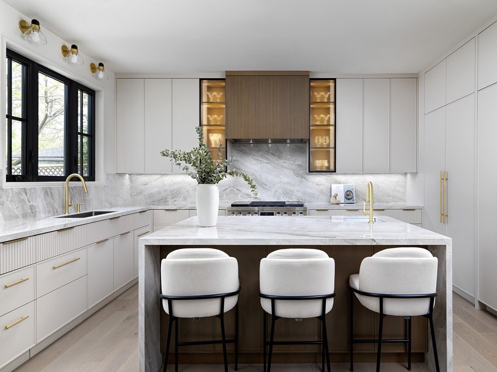 A kitchen with white cabinets, marble counter tops, stools and a large island in Angelene St by Oakroots Construction