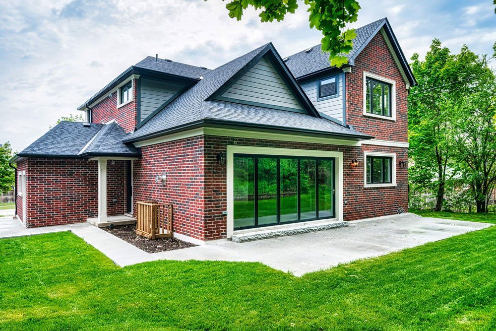 A large brick house with a lot of windows is sitting on top of a lush green lawn in Hazelridge Dr by Oakroots Construction.