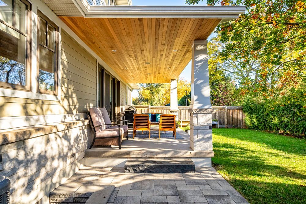 There is a covered patio with chairs and a grill in the backyard of a house on Tansley Drive by Oakroots Construction