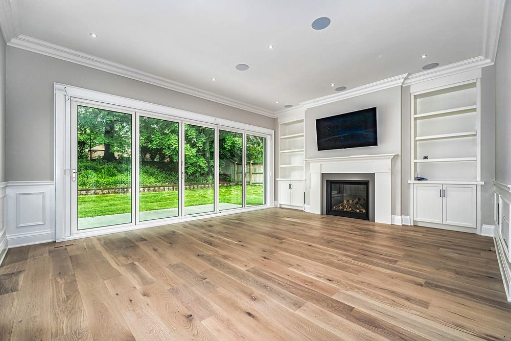 An empty living room with hardwood floors, sliding glass doors, a fireplace and a flat-screen tv in Hazelridge Dr by Oakroots Construction