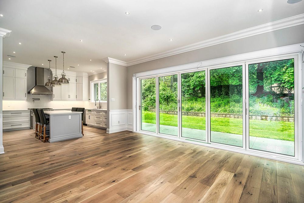 An empty living room with hardwood floors and sliding glass doors leading to a kitchen in Hazelridge Dr by Oakroots Construction