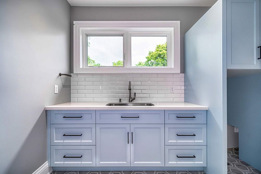 A kitchen with white cabinets, drawers, a sink and a window in Hazelridge Dr by Oakroots Construction