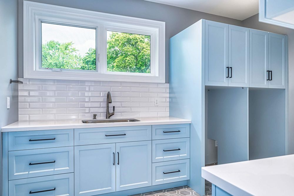 A kitchen with blue cabinets, white countertops, a sink and a window in Hazelridge Dr by Oakroots Construction