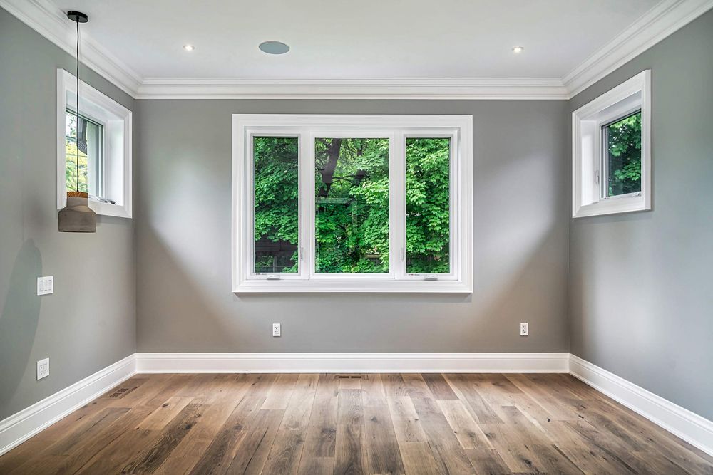 An empty room with hardwood floors and three windows in Hazelridge Dr by Oakroots Construction