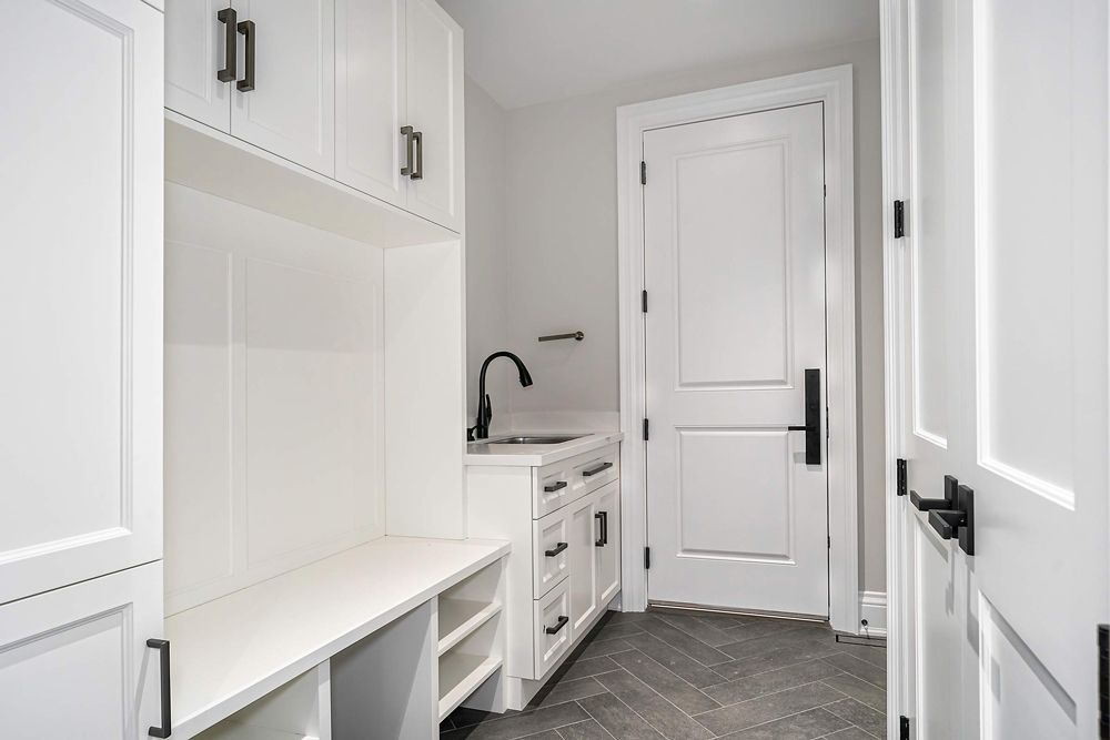 A laundry room with white cabinets and a sink in Hazelridge Dr by Oakroots Construction