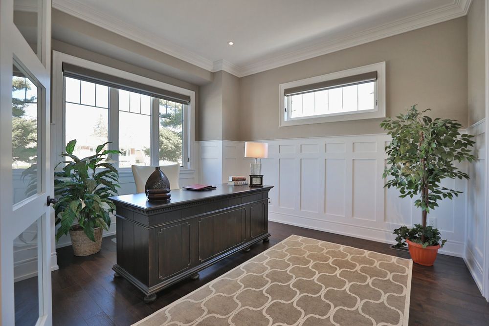 A home office with a desk , rug , plant and window.