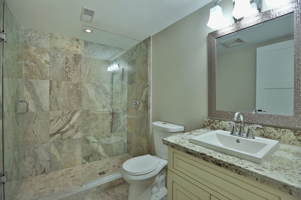 A bathroom with a toilet , sink , mirror and walk in shower.