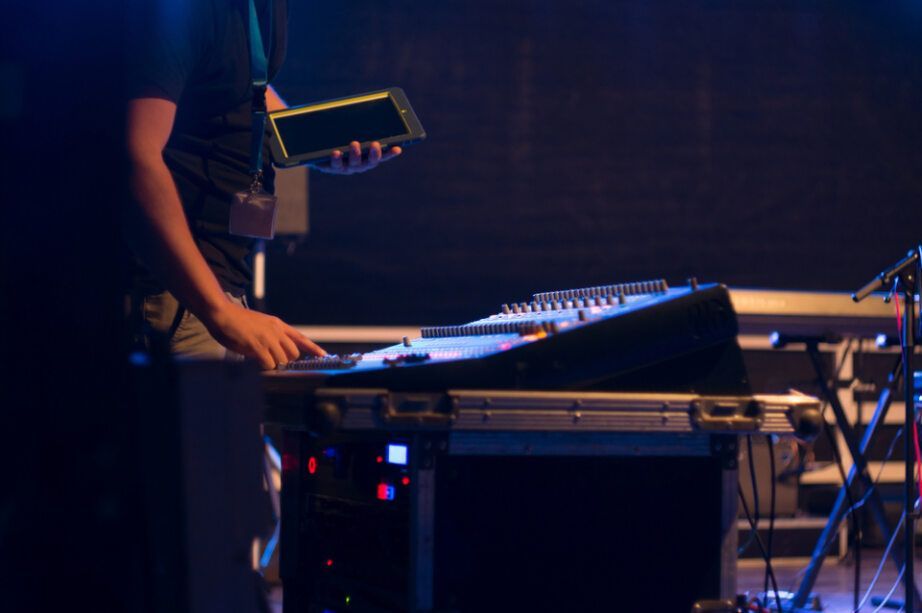 A Person with A Tablet Operates a Soundboard on Stage in A Darkened Setting — Pacific Telephone & Data In Cardiff, NSW