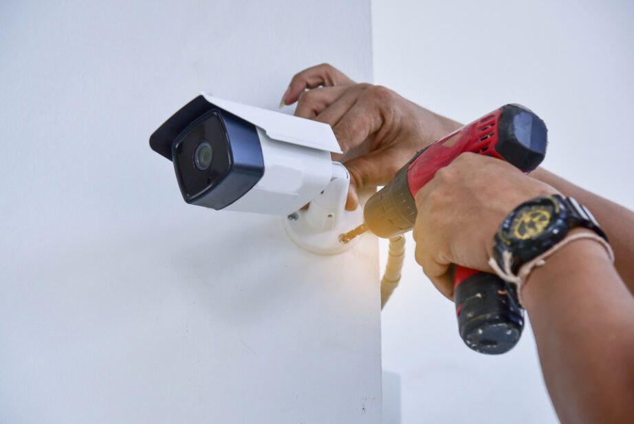 Hands Installing a Security Camera on A White Wall with A Red Drill — Pacific Telephone & Data in Lake Macquarie, NSW