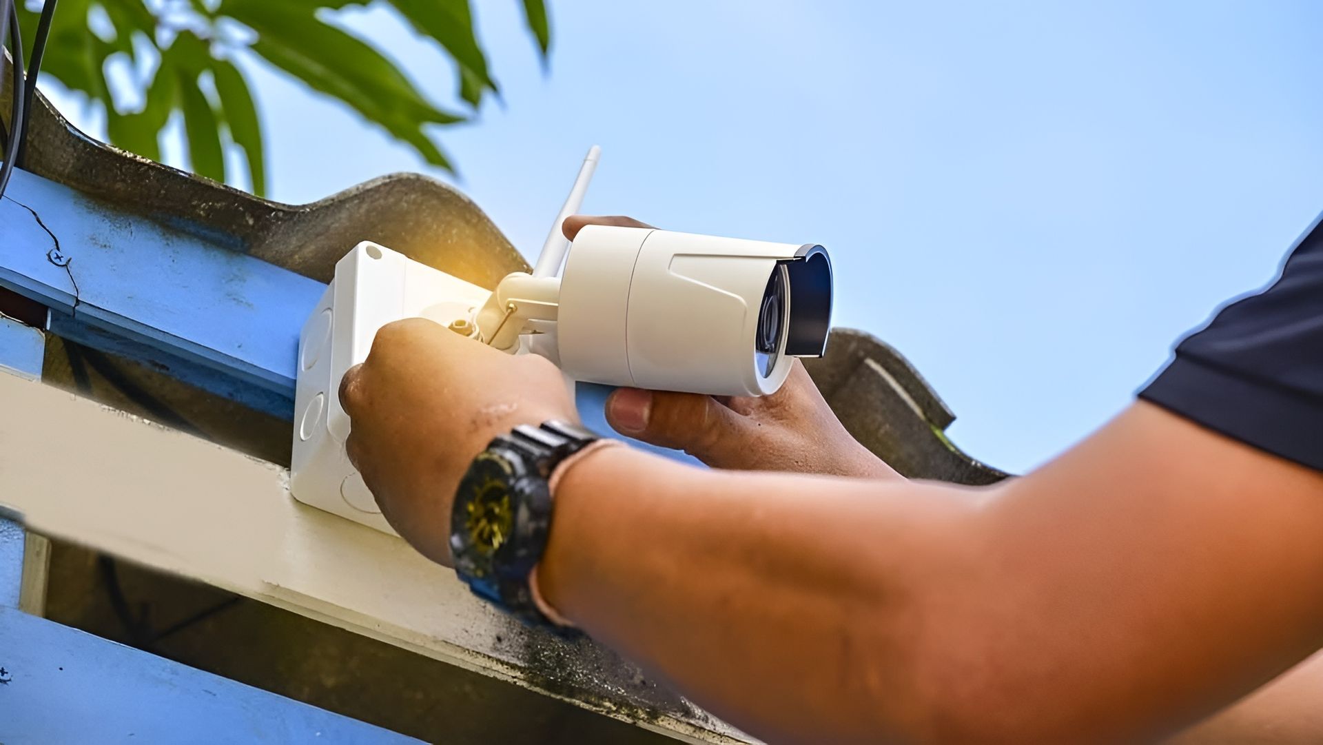Person Installing a Security Camera on A Blue Metal Surface Outdoors — Pacific Telephone & Data In Cardiff, NSW